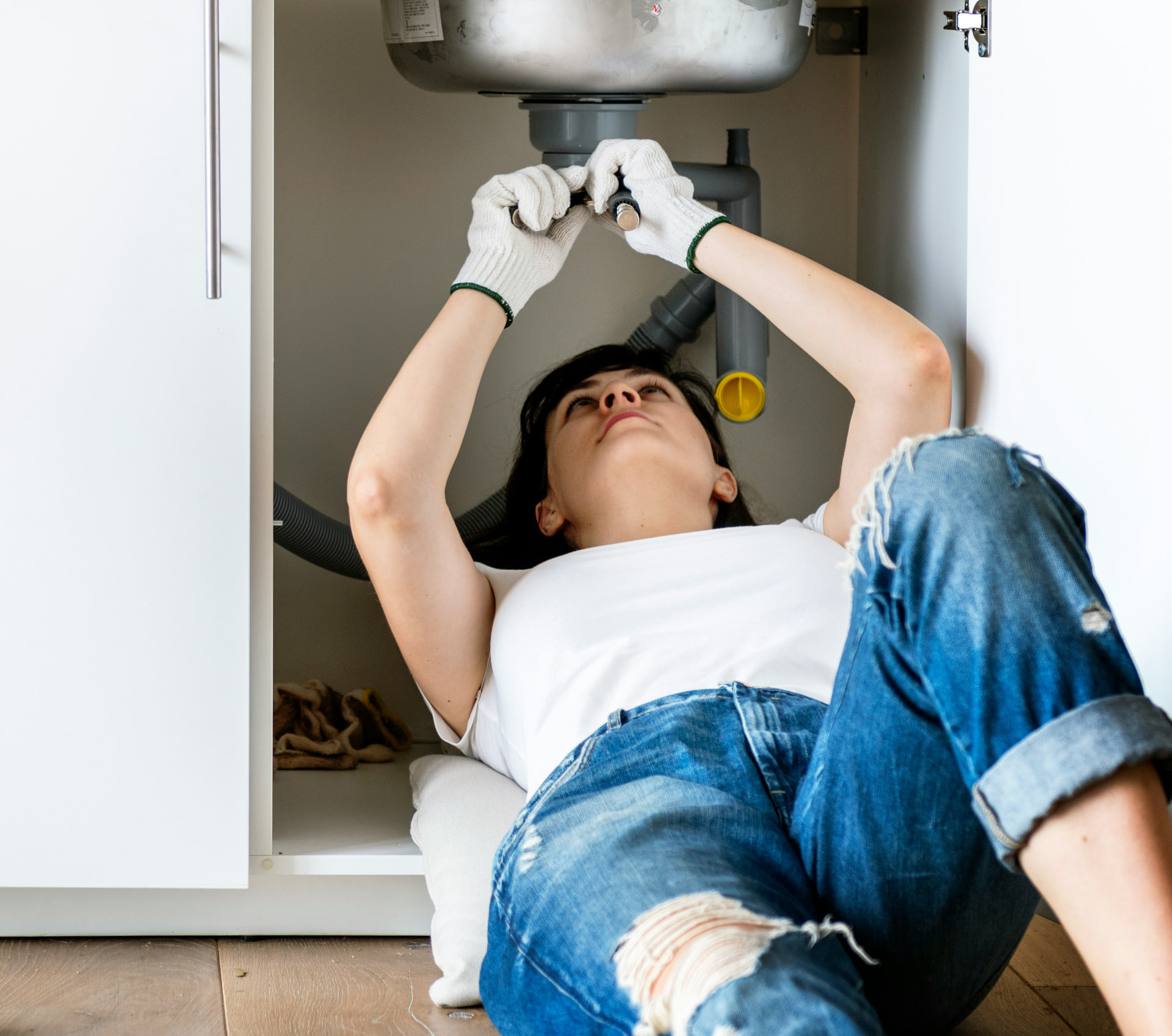 Person fitting plumbing hardware under a kitchen sink